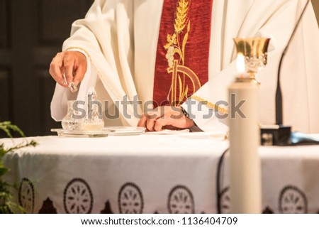Hands of a catholic priest in red gown on altar, candle in foreground