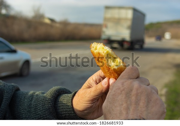 Hands of Caucasian hungry senior\
driver holding half of fried patty against road with\
cars