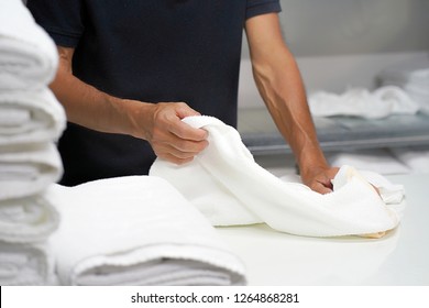 Hands of caucasian male laundry hotel worker folds a clean white towel. Hotel staff workers. Hotel linen cleaning services.