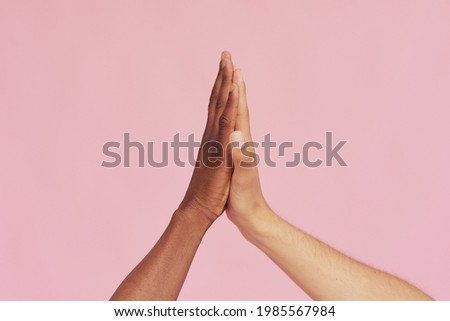 Hands of Caucasian man and black African American giving each other five on pink background. The concept of racism and all lives matter 商業照片 © 