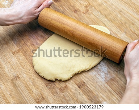 Hands of a caucasian woman is rolling out the dough with a rolling pin on a wooden board. Close-up.