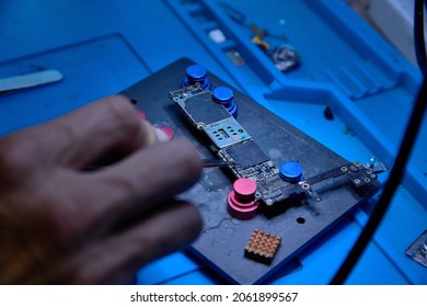 Hands of cellphone technology device maintenance engineer work on chipset pins of removed microprocessor from smartphone motherboard with tweezers. Close-up macro photo, Selective focus
