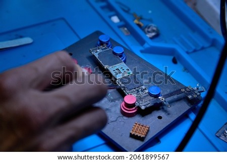Hands of cellphone technology device maintenance engineer work on chipset pins of removed microprocessor from smartphone motherboard with tweezers. Close-up macro photo, Selective focus