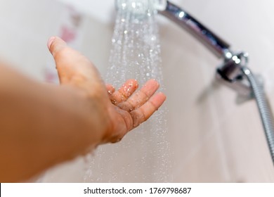 hands check the temperature of the shower water. a man's hand under a stream of water selective focus