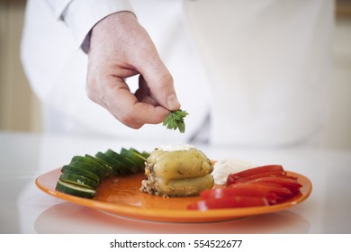 Hands of a chef adding some parsley to a stuffed pepper.