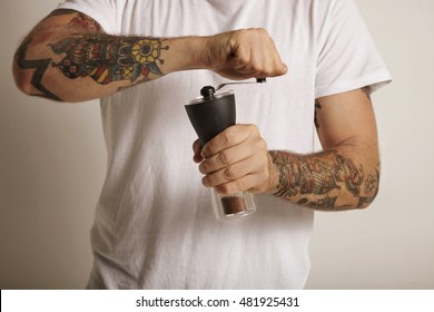 Hands And Chest Of A Tattooed Young Man Grinding Coffee In A Manual Burr Grinder