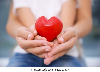 Hände von Kindern und Erwachsenen mit rotem Herzen, Nahaufnahme