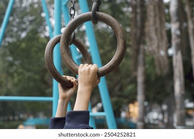 Hands of a child gripping wooden gymnastics rings in a playground - Powered by Shutterstock