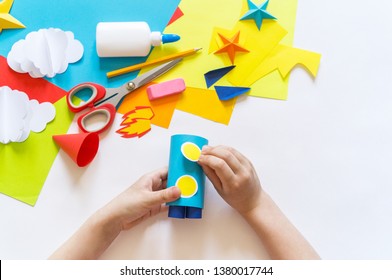 Hands Of The Child Make A Paper Craft Rocket. Cosmos Clouds And Stars Colored Paper. The Creative Process. Kindergarten And School Development. Master Class.