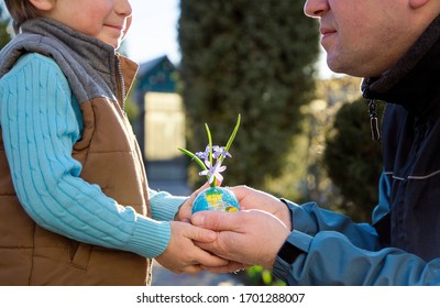 in hands of child and man (father and son) earth is in miniature, ball in  form of globe from which small flowers of chionodoxa grow. Earth Day Concept, Eco-Education, Environmental awareness and care