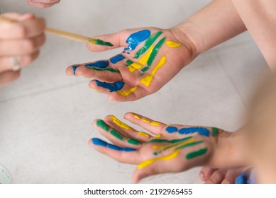 Hands Of A Child In Paint. Kids Hands Covered With Paint Top View.  Teacher Works With Children According To The Montessori Method And Paints Their Hands. 