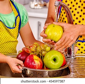 Hands of children washing fruits at kitchen. Water pouring on fruit.