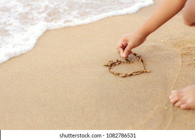 Hands of children writing a heart on beach.