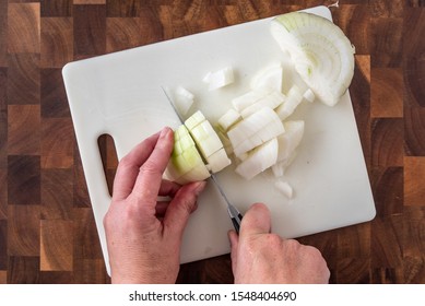 Woman’s hands chopping an onion, white cutting board on wood butcher block
