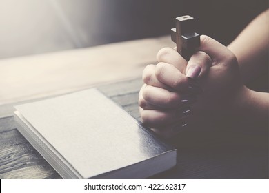 Hands of Christian woman praying on wooden desk