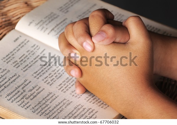 Hands clasped in prayer\
on Holy Bible