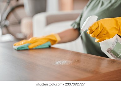 Hands, cleaning and spray on a wooden table for hygiene, disinfection or to sanitize a surface in a home. Gloves, bacteria and product with a woman cleaner in the living room for housework or chores - Powered by Shutterstock