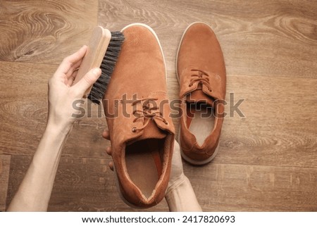 Hands cleaning suede shoes with a brush on wooden floor. Top view. Shoe care Imagine de stoc © 