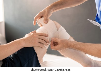 Hands Of Clinician Wrapping Right Knee Of Patient With Flexible Bandage During Medical Procedure Before Rehabilitation Physical Training