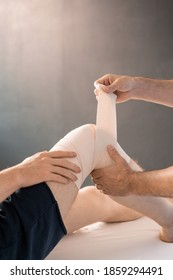 Hands Of Clinician Wrapping Right Knee Of Sick Man With Flexible Bandage During Medical Procedure Before Rehabilitation Physical Training