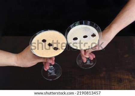 Hands clinking classes with espresso martini on  black background