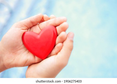 Hands close up holding red heart with blue background