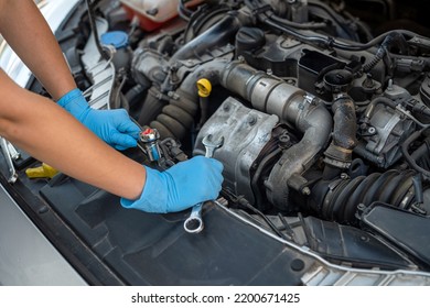 Hands Close Up Of A Smiling Young Female Mechanic Performing Diagnostics On A Car In An Auto Repair Shop. Woman Mechanic. Woman's Hands Under The Hood