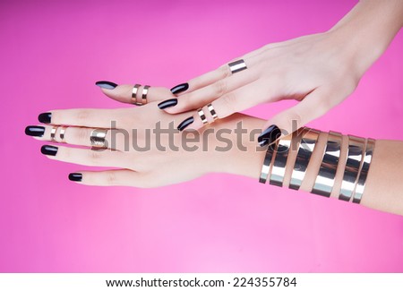 Hands close up of young woman with black manicure wearing gold bracelet and knuckle rings