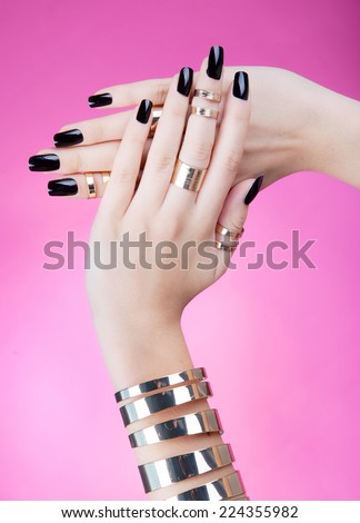 Hands close up of young woman with black manicure wearing gold bracelet and knuckle rings