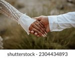 Hands close-up of boho couple in nature holding hands and walking, hugging having fun for their engagement photo session.