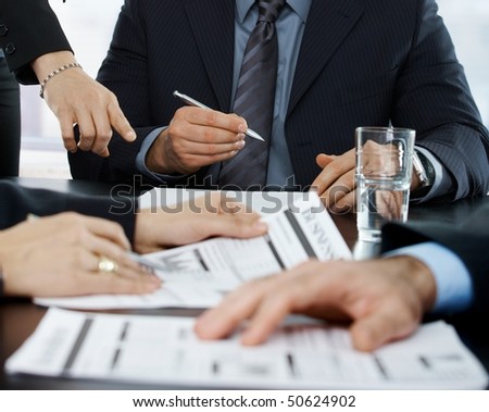 Hands in closeup at businessmeeting focusing on business documents and pointing at papers to sign.