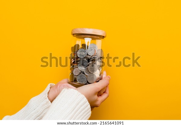 Hands and coins in a savings jar money saving\
on yellow background money saving concept Plant a plan to save\
money for children.