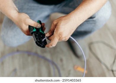 Hands connect the cable with a tool. Electrical work, technical style, light background. Conducting the Internet.