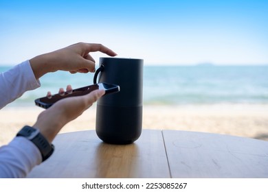 Hands connecting cell phone with bluetooth speaker with beach background, Vacation activity.