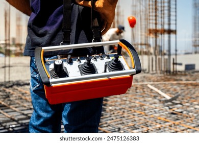 Hands of a construction worker or engineer operating a remote control of construction equipment at a construction site. Close-up view