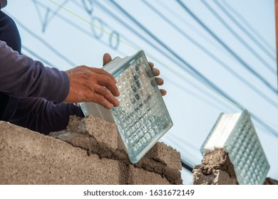 Hands of construction worker installing glass blocks on cement wall at construction site with electric lines background 
