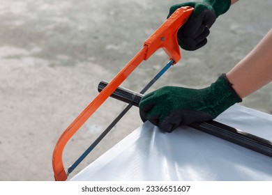 Las manos de un trabajador de la construcción que usa guantes están usando una motosierra para cortar un trozo de tubo de aluminio.