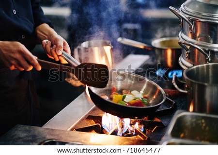 Hands of cook frying vegetables on pan