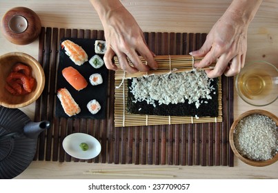 hands cooking sushi with rice, salmon and nori