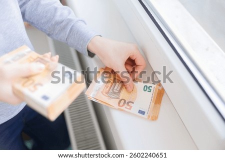 Hands counting euro banknotes while placing them on a radiator, symbolizing the rising utility costs and financial burden of energy bills during colder months.