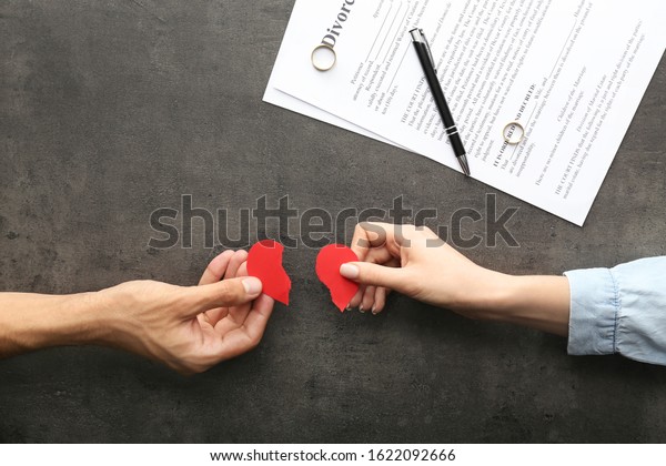 Hands of couple with broken heart on dark\
background. Concept of\
divorce