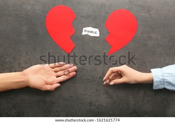 Hands of couple with broken heart and\
wedding rings on dark background. Concept of\
divorce