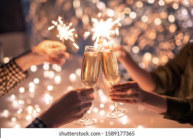 Hands of couple clinking with flutes of champagne and their friends holding sparkling bengal lights - Powered by Shutterstock