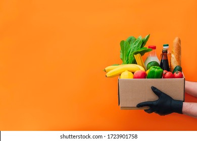 The hands of courier in protective gloves delivers box of different food on an orange background. Food delivery during virus outbreak. Safe home delivery. Takeout meal.  - Shutterstock ID 1723901758