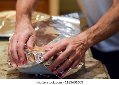 Hands Covering Casserole Dish With Aluminum Foil To Back In Oven