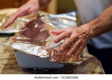 Hands Covering Casserole Dish With Aluminum Foil To Back In Oven