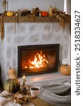 Hands in cozy sweater holding warm cup of tea with pumpkin and autumn leaves on table on background of burning fireplace. Autumn hygge. Thanksgiving and Halloween.