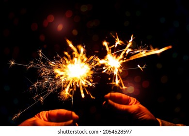 Hands with cracking Bengal light. Bright festive fireworks in the dark sky. Sparkling fire, flashes, illumination. Celebrating the national holiday, New Year.