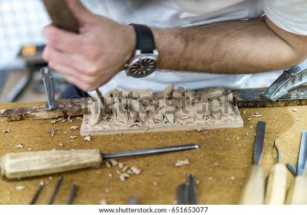 Hands of craftsman carve with a gouge in the\
hands on the workbench in\
carpentry