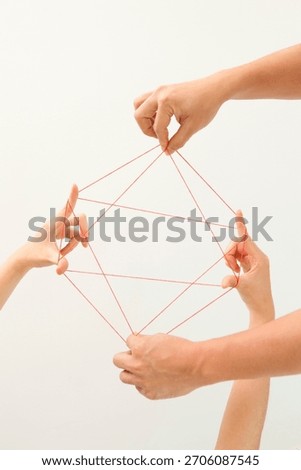Hands creating a geometric pattern by pulling red string in a playful activity